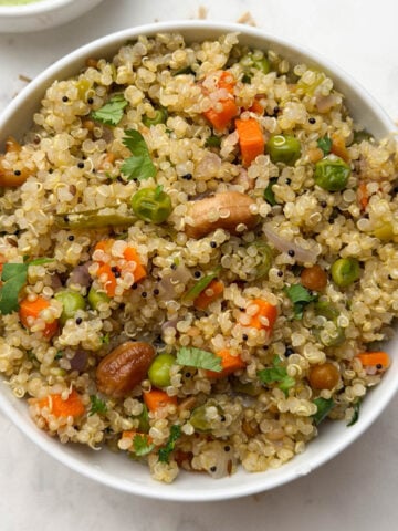 Quinoa upma served in a white bowl with coconut chutney on the side.