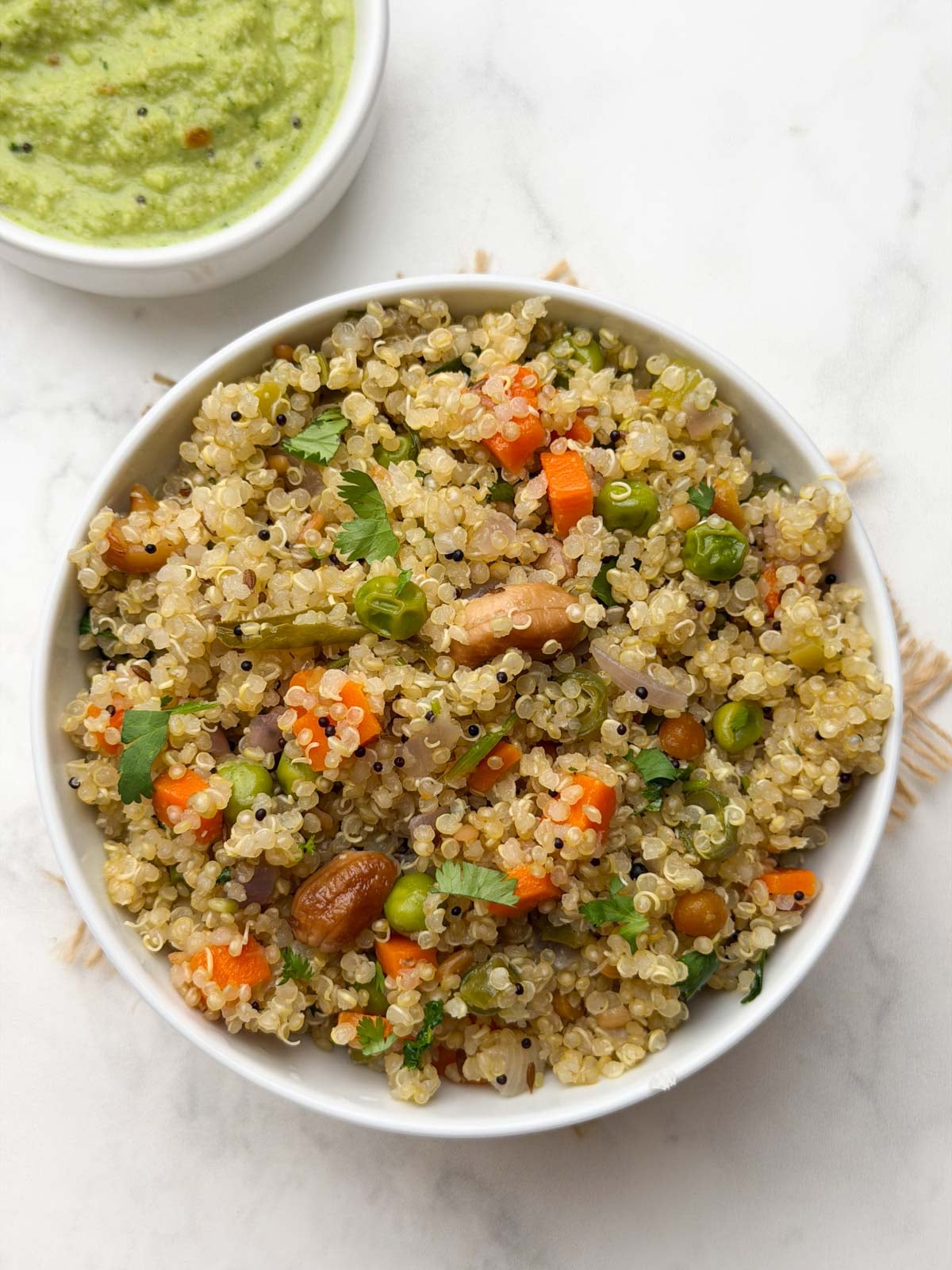 Quinoa upma served in a white bowl with coconut chutney on the side.