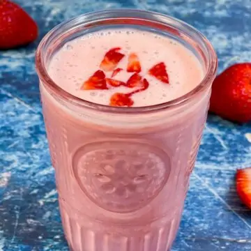 strawberry lassi served in a glass topped with chopped strawberry