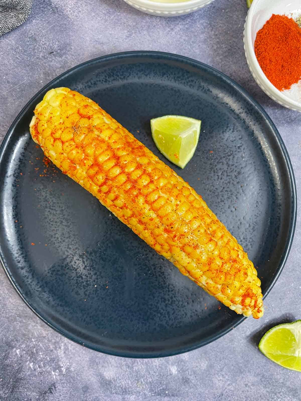 spiced corn on the cob on a plate with spices and lemon wedge on the side