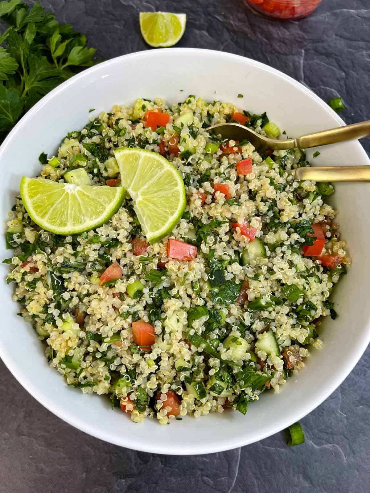 Quinoa Tabbouleh Salad served in a bowl with two spoons topped with lemon wedges
