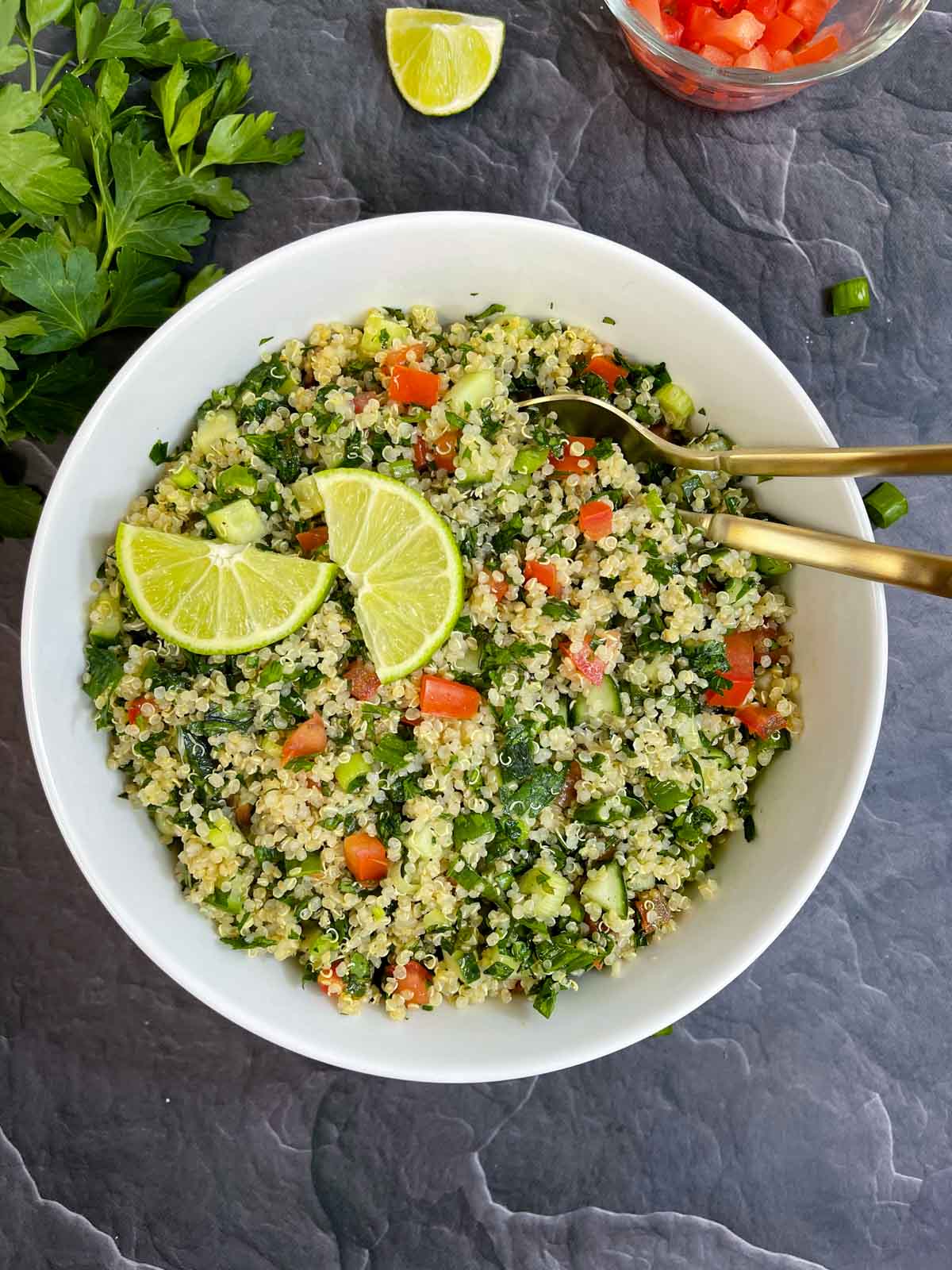 Quinoa Tabbouleh Salad served in a bowl with two spoons topped with lemon wedges