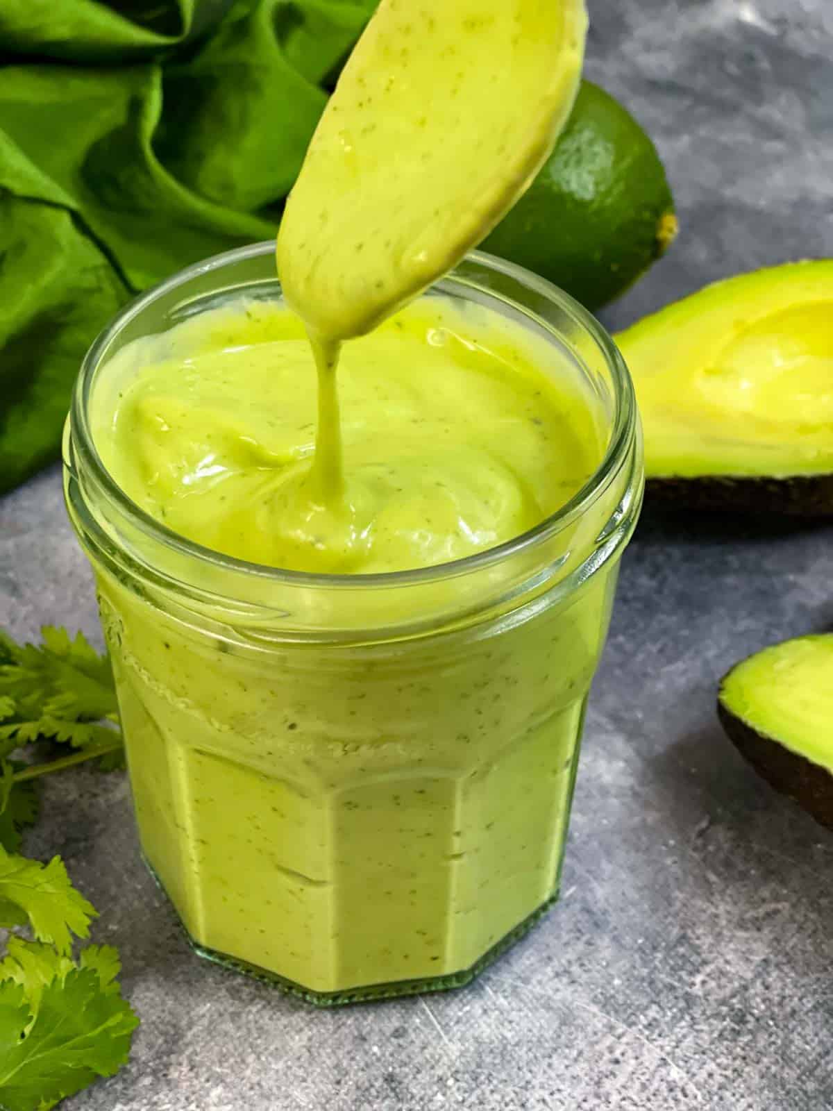 Creamy avocado dressing in a jar with sauce dripping from a spoon