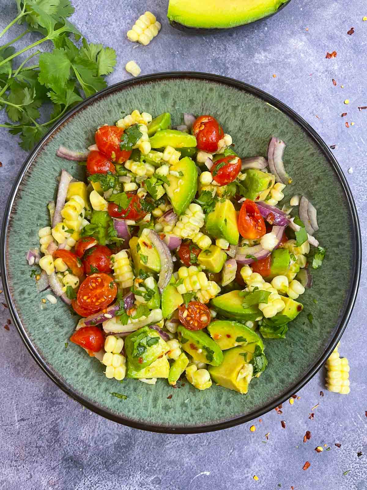 avocado corn tomato salad served in a bowl with cilantro and cut avocado on the side