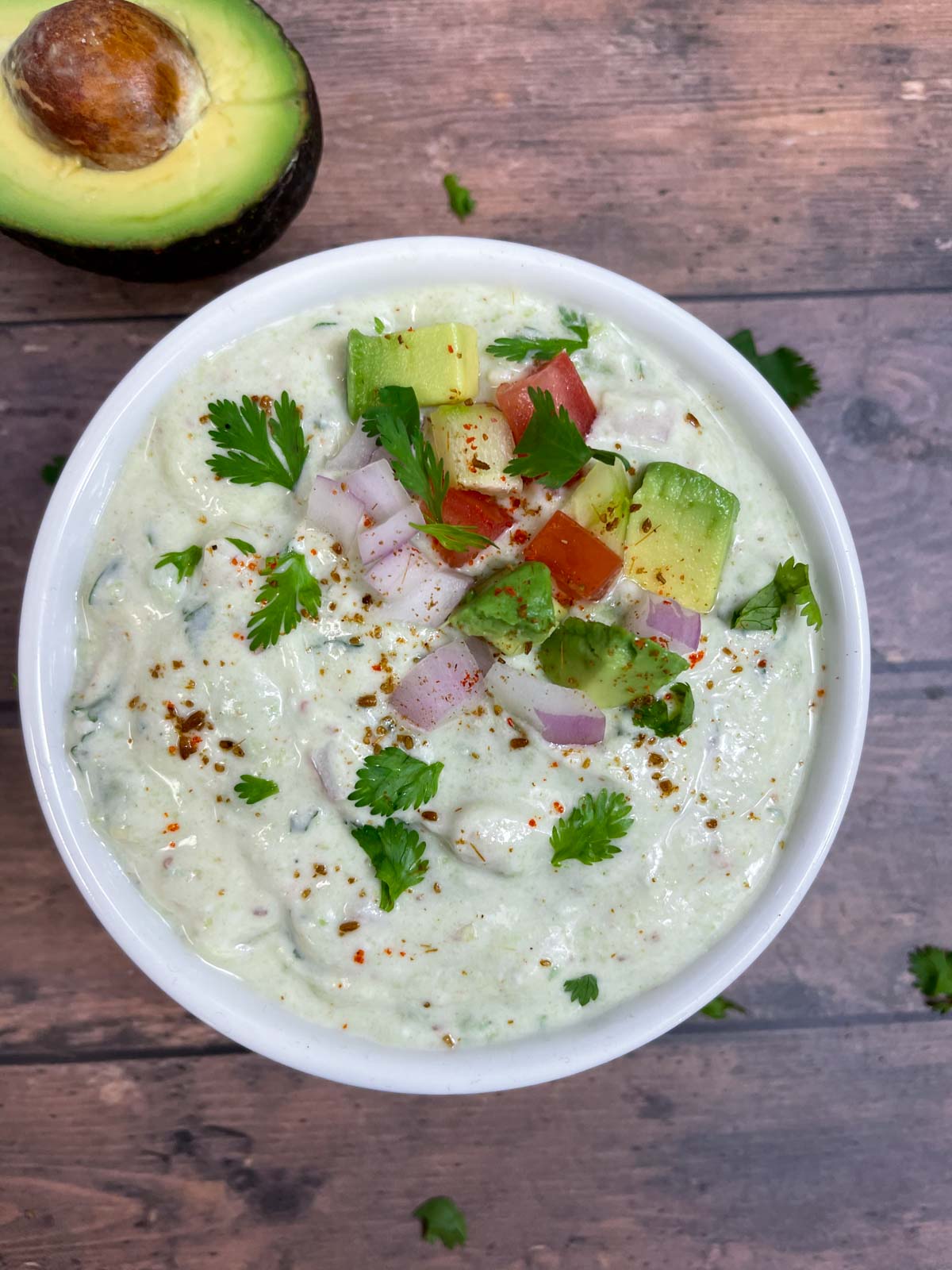 avocado raita served in a bowl topped with diced avocado, cucumber, onion, tomato and spices