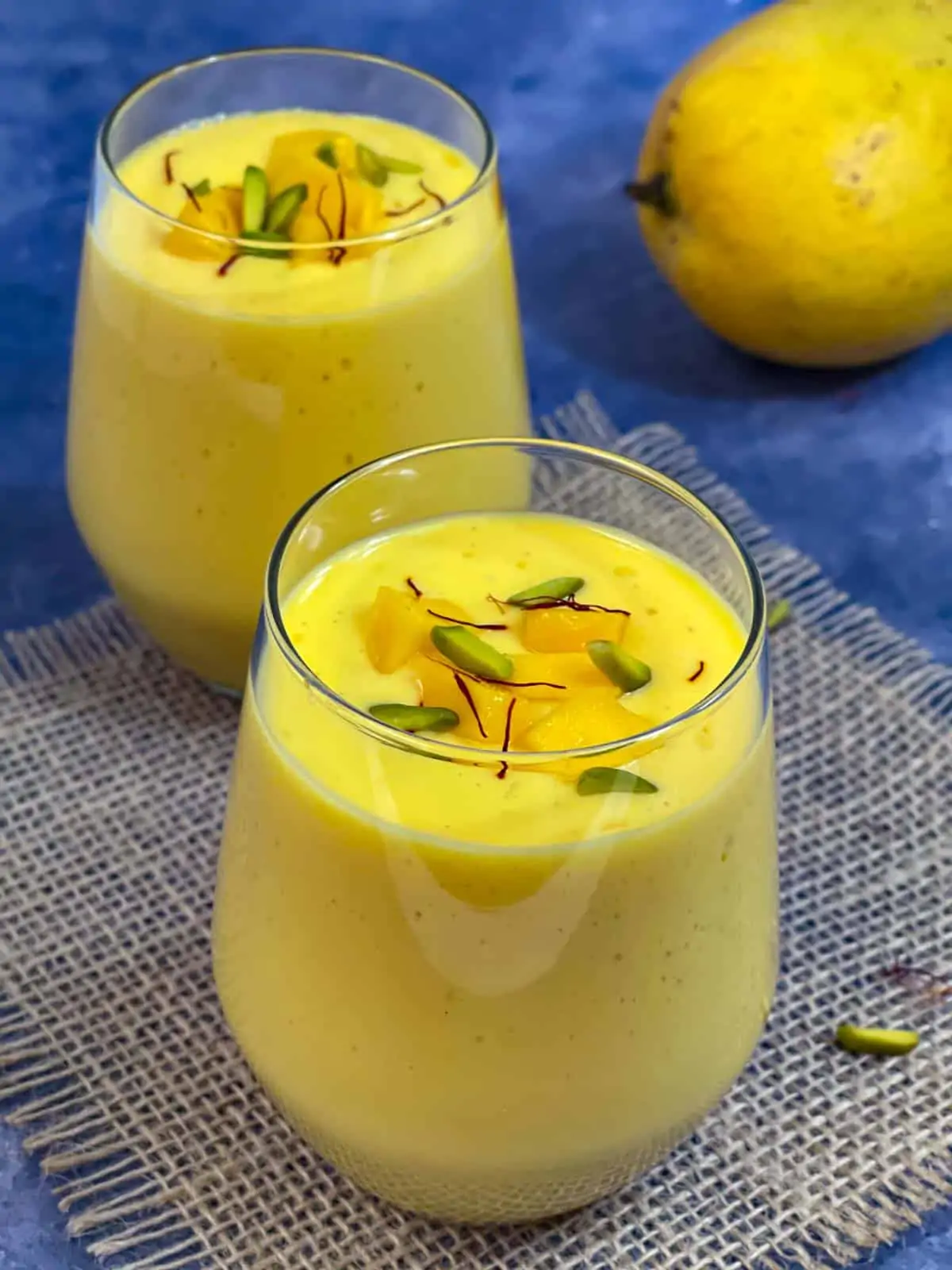 Mango lassi served in a serving glass topped with pistachios and saffron
