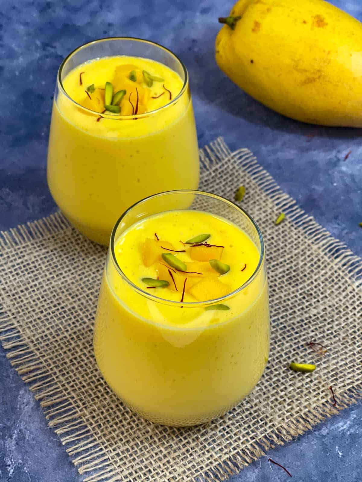 Indian Mango lassi served in a serving glass garnished with nuts, chopped mango and saffron