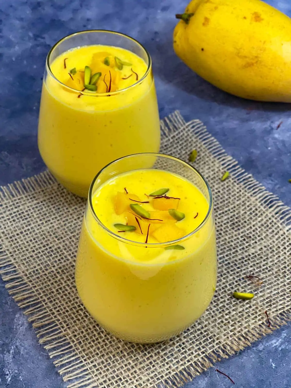 Indian Mango lassi served in a serving glass garnished with nuts, chopped mango and saffron