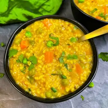Instant pot Indian masala oats served in a bowl with spoon garnished with cilantro