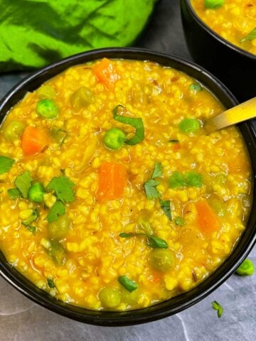 Instant pot Indian masala oats served in a bowl with spoon garnished with cilantro