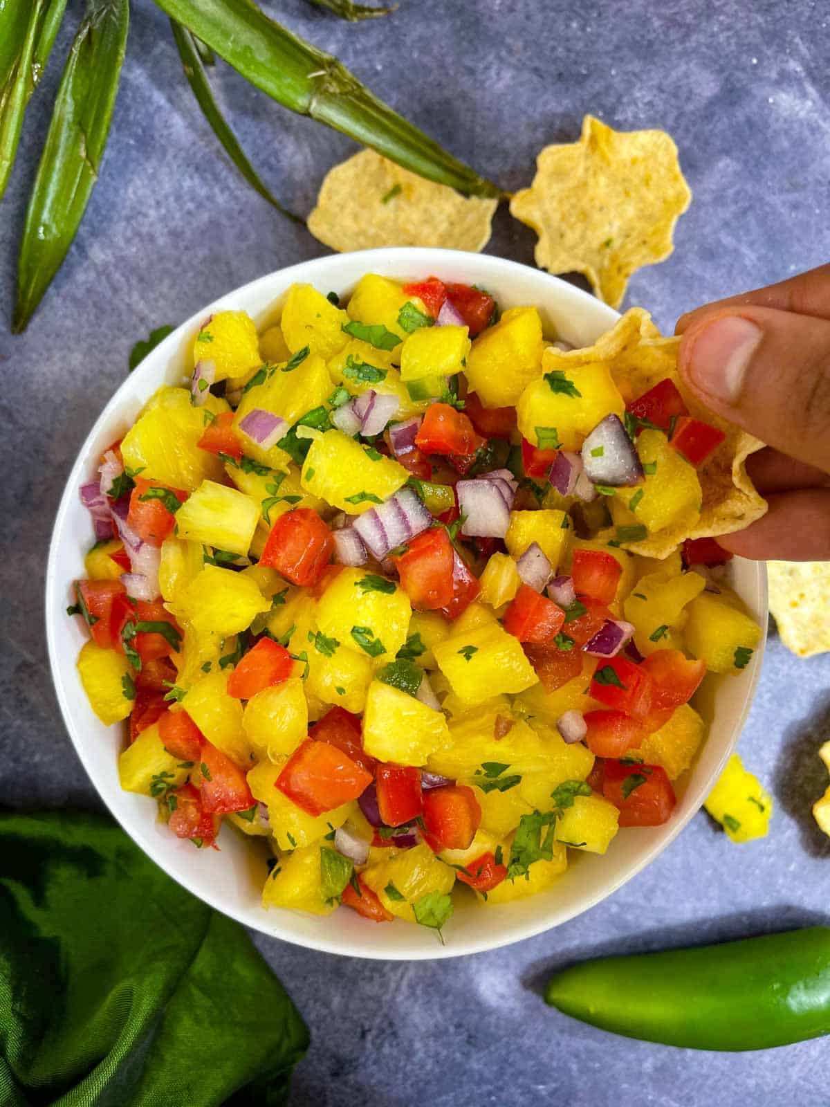 Pineapple salsa served in a bowl and scooping the salsa with chips