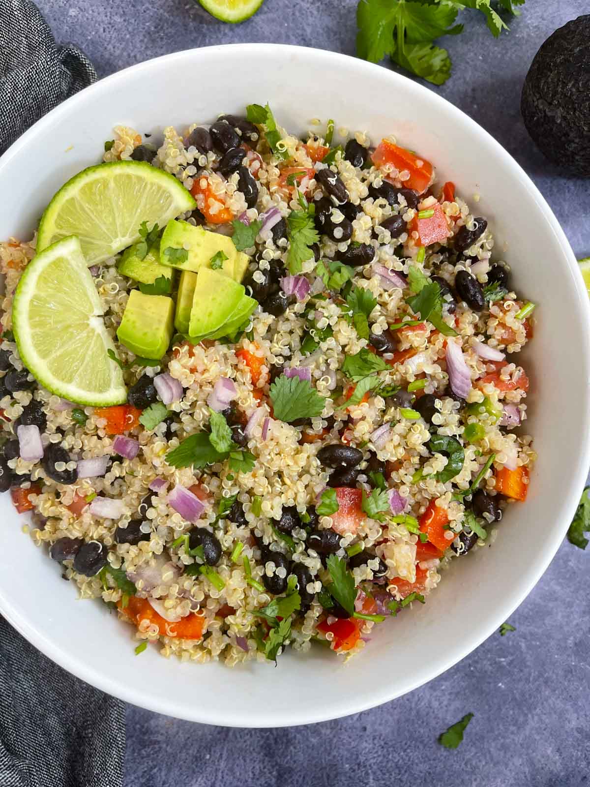 quinoa and black bean salad served in a bowl topped with avocado and lemon wedges