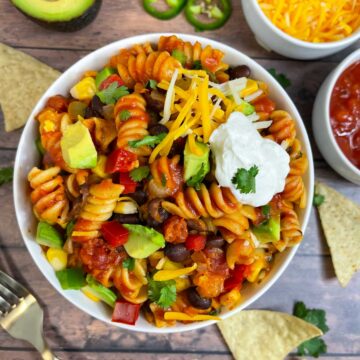 taco pasta served in a bowl topped with sour cream, avocado, cheese and cilantro