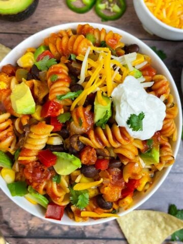 taco pasta served in a bowl topped with sour cream, avocado, cheese and cilantro