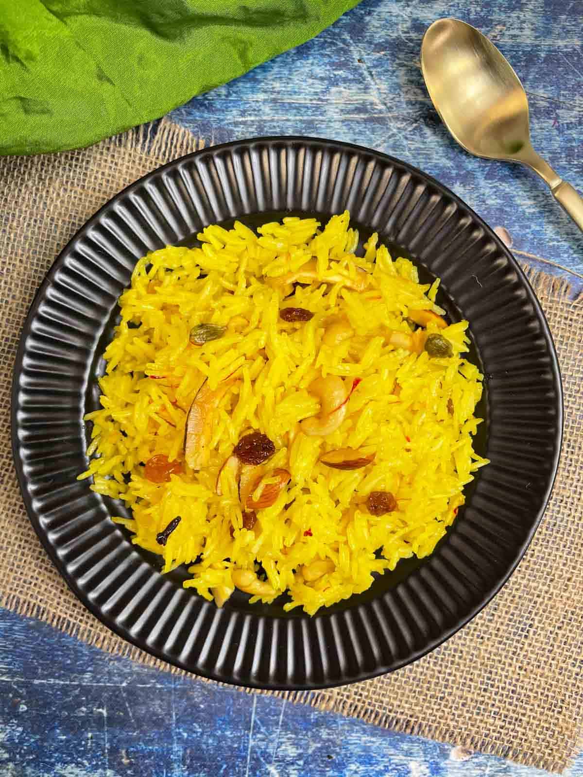 zarda pulao (meethe chawal/sweet rice) served in a plate with spoon on the side