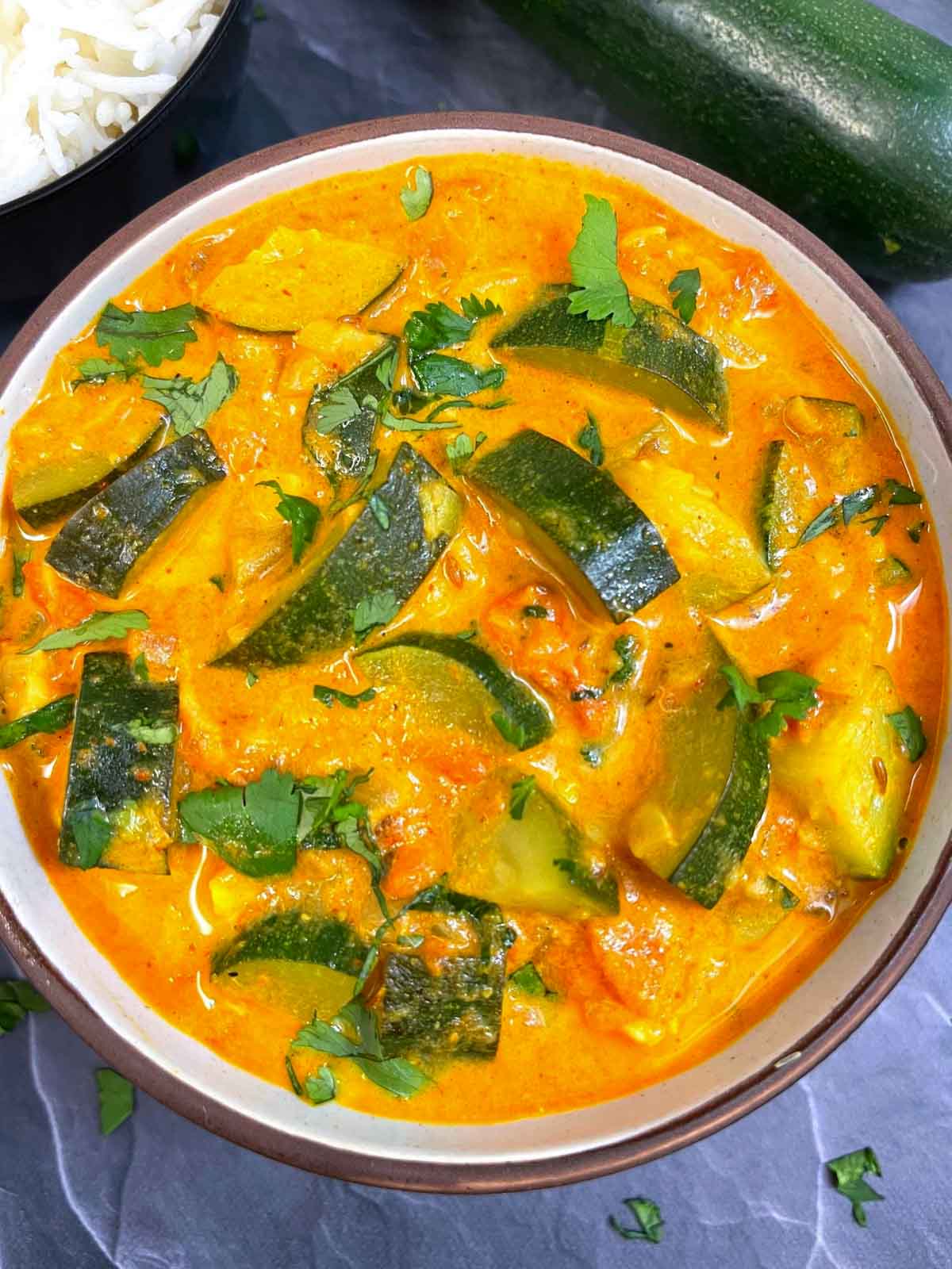 zucchini curry served in a bowl garnished with cilantro with side of rice