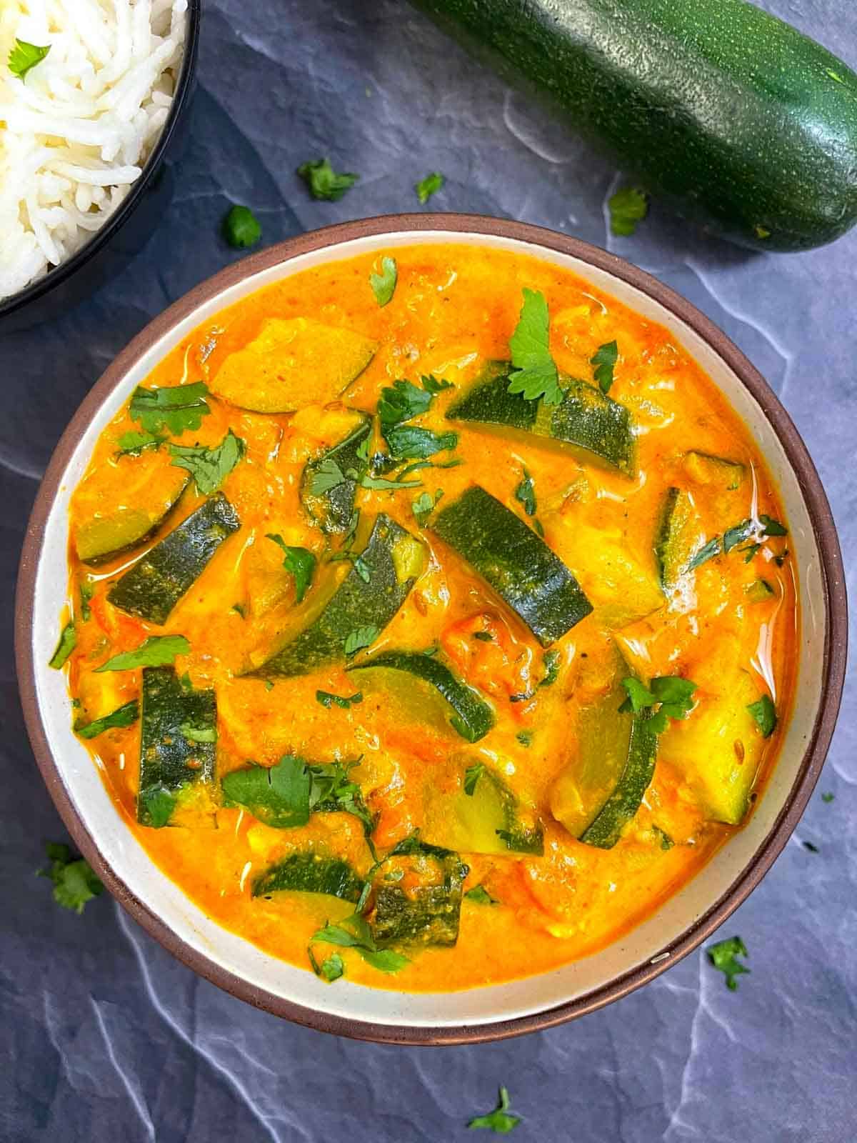 zucchini curry served in a bowl garnished with cilantro with side of rice