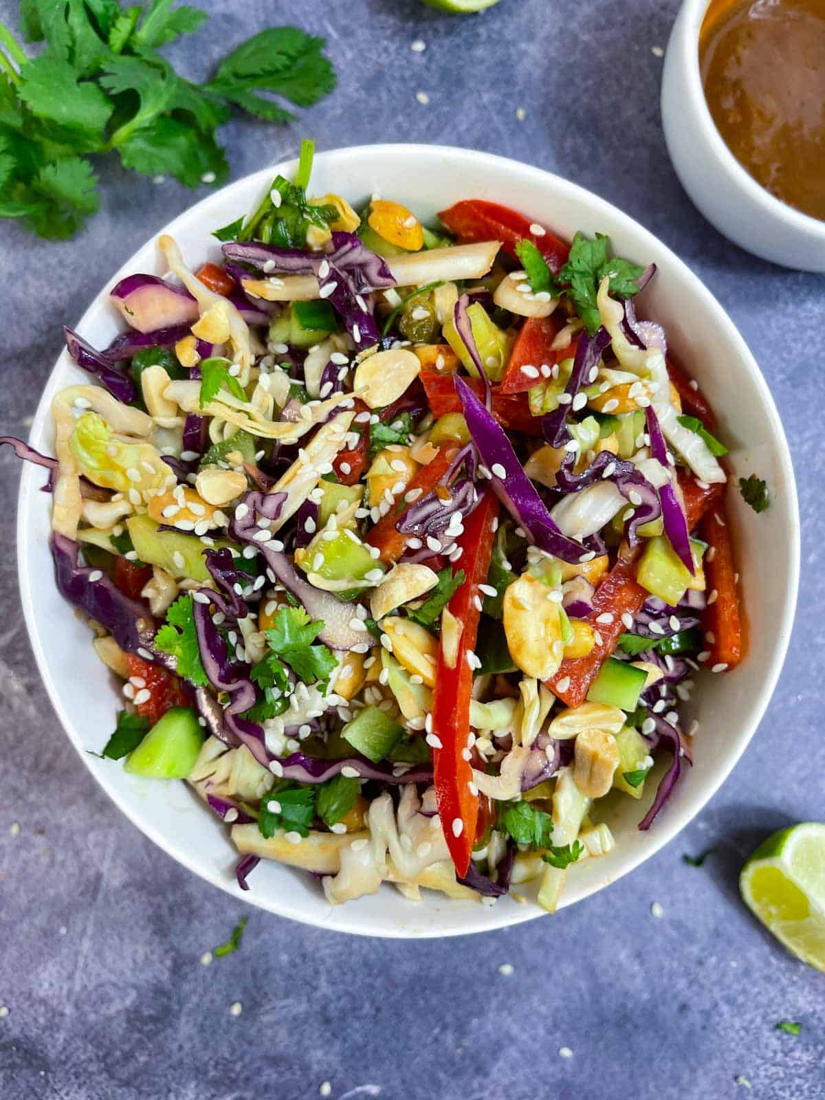 Thai Salad with delicious creamy Peanut Dressing served in a bowl garnished with sesame seeds and peanuts with side of dressing and lemon wedge