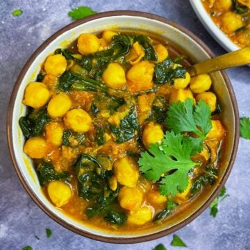 chickpea curry with spinach served in a bowl garnished with cilantro and has a spoon