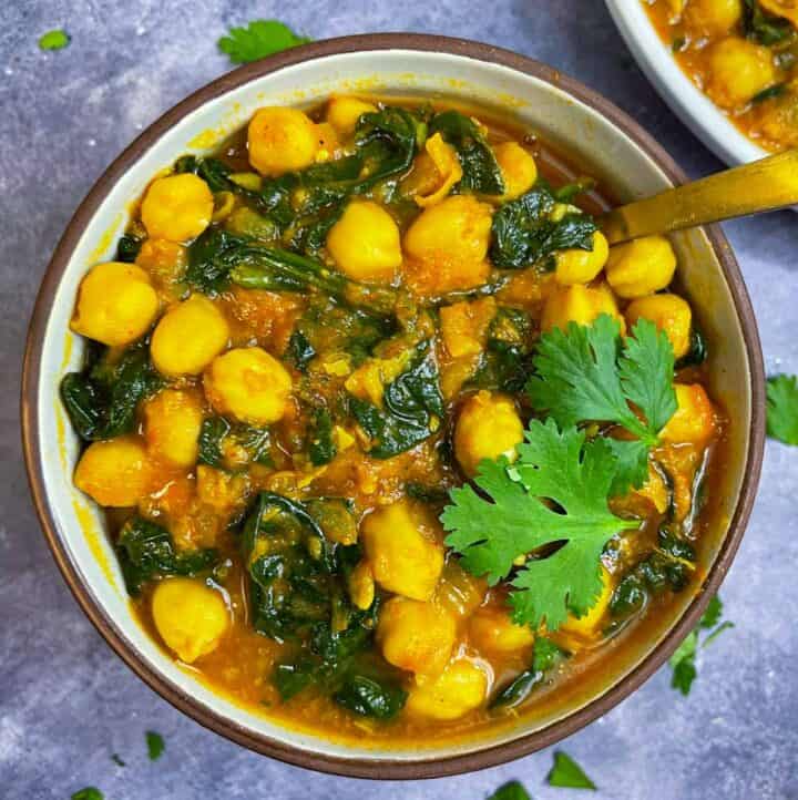 chickpea curry with spinach served in a bowl garnished with cilantro and has a spoon