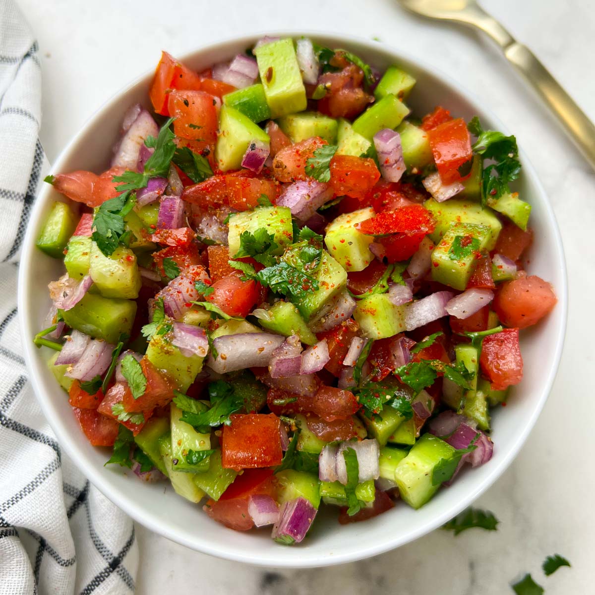 kachumber salad served in a bowl with spoon on the side