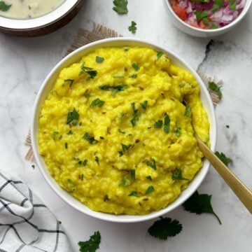 moong dal khichdi served in a bowl with a spoon and kadhi and salad on the side