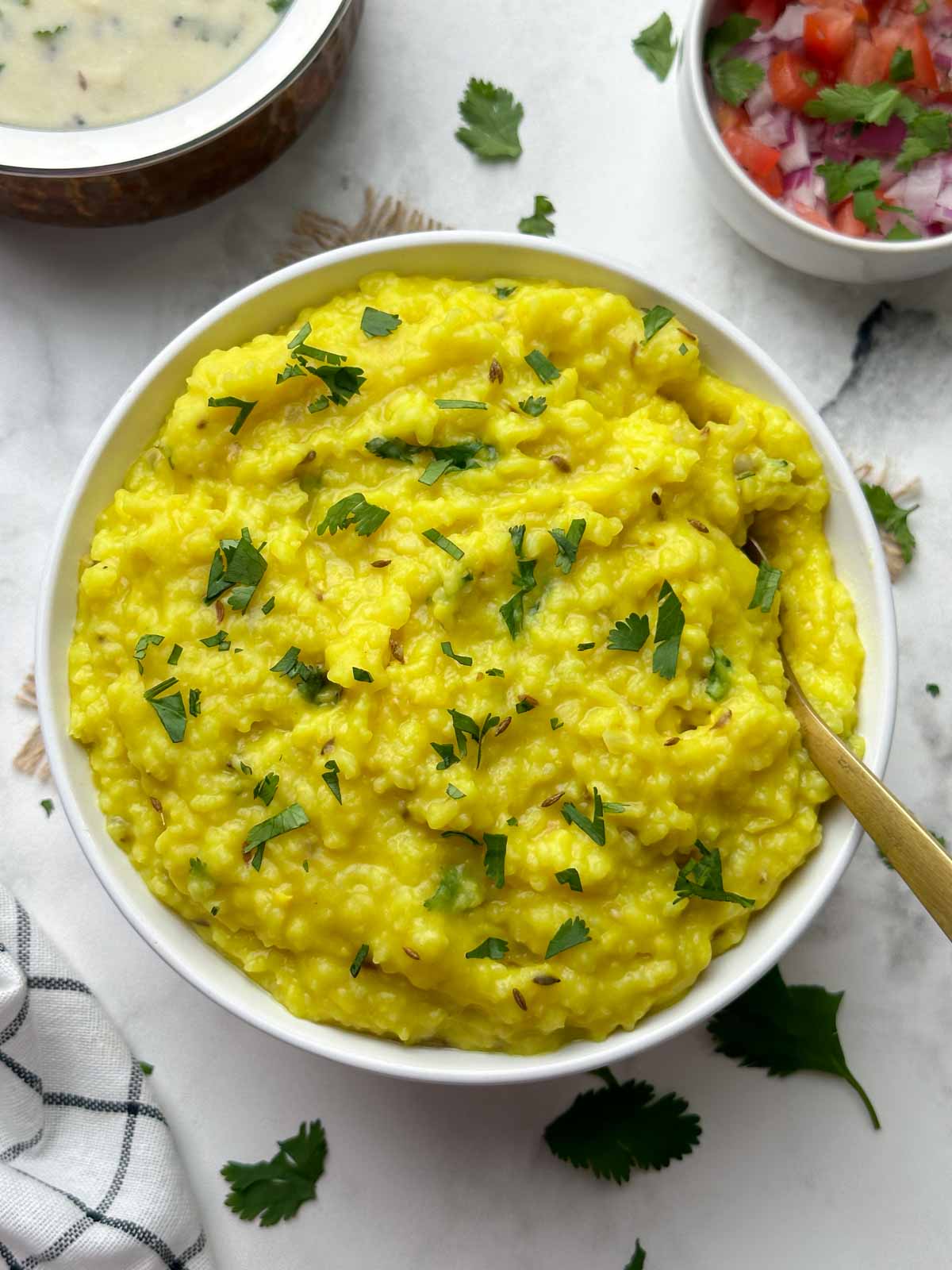 moong dal khichdi served in a bowl with a spoon and kadhi and salad on the side