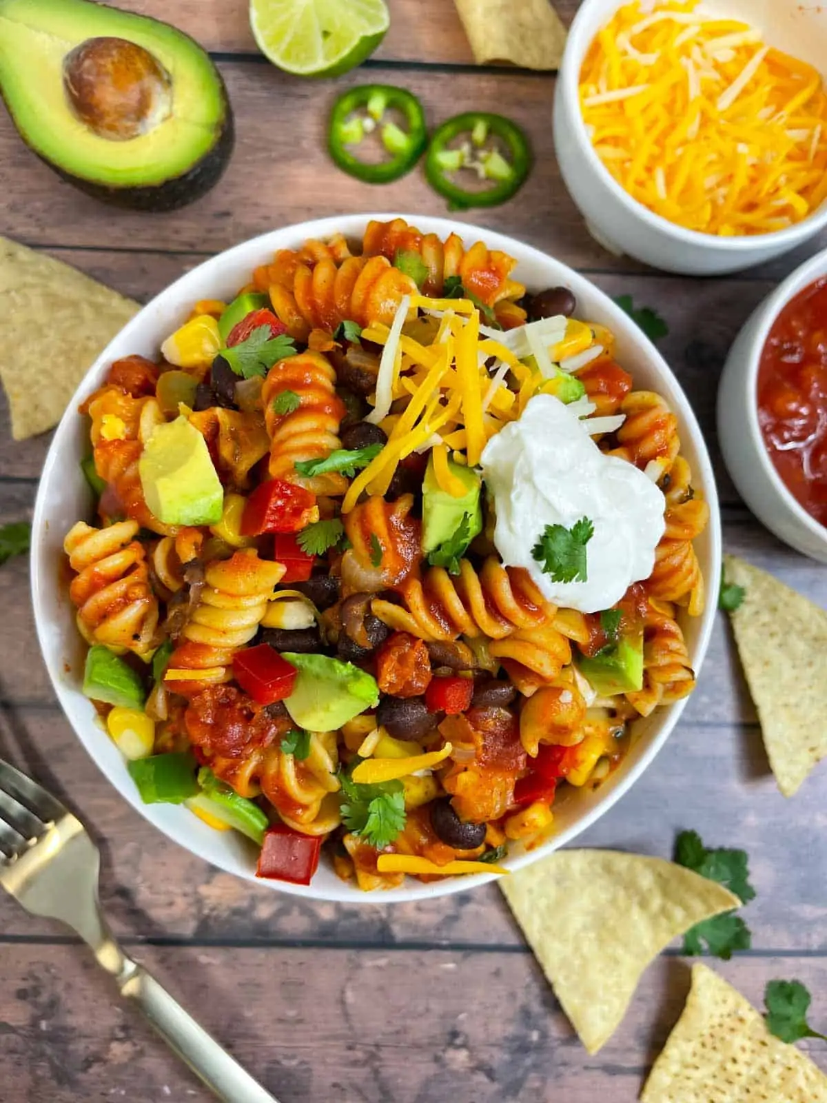 taco pasta served in a bowl topped with sour cream, avocado, cheese and cilantro