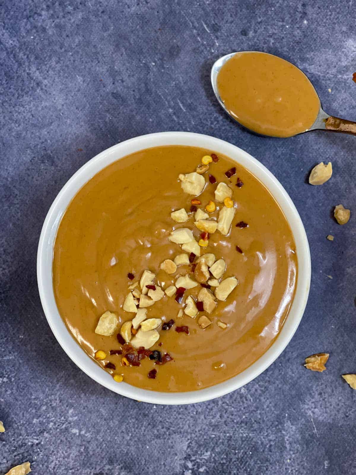 Thai peanut sauce {dressing} served in a bowl topped with roasted crushed peanuts and chili flakes with spoon full of the saue on the side