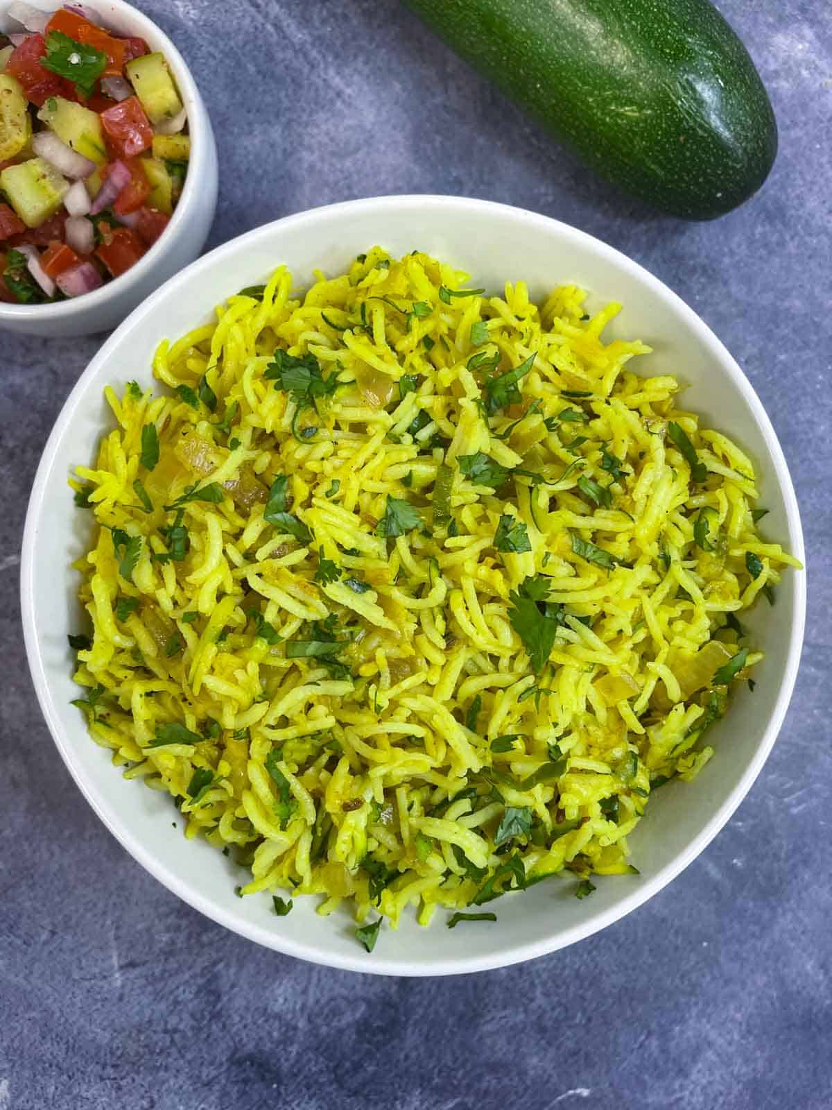 zucchini rice pilaf served in a bowl garnished with coriander leaves with side of salad