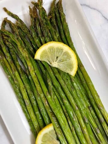 roasted air fryer asparagus served on a plate with two lemon wedges