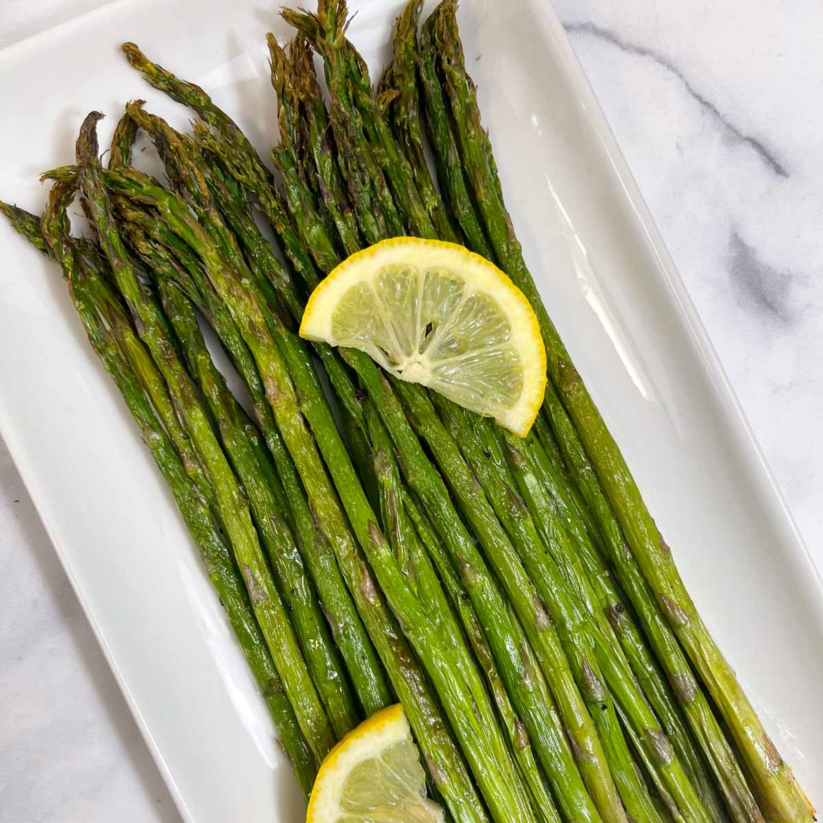 roasted air fryer asparagus served on a plate with two lemon wedges