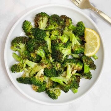 air fryer roasted broccoli served on a plate with lemon wedge on the side.