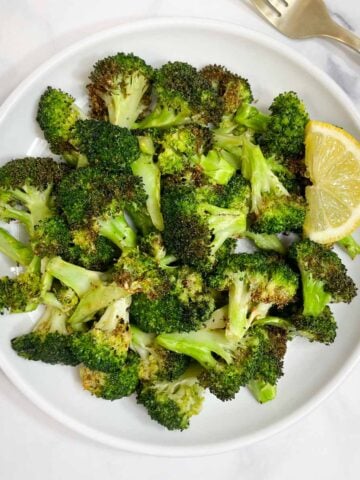 air fryer roasted broccoli served on a plate with lemon wedge on the side.