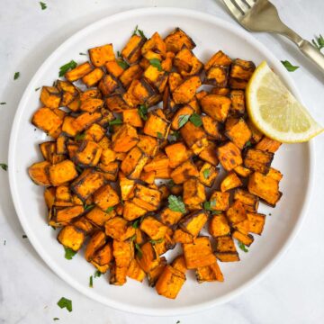air fryer roasted sweet potato cubes served on a plate garnished with cilantro with lemon wedge on the side