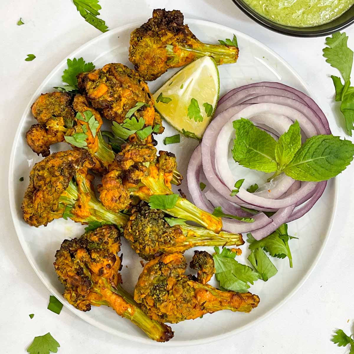 tandoori broccoli tikka served on a plate with lime wedge, onions and mint chutney collage