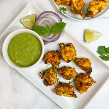 air fryer tandoori gobi served on a plate with onions, green chutney and lemon wedges