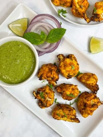 air fryer tandoori gobi served on a plate with onions, green chutney and lemon wedges