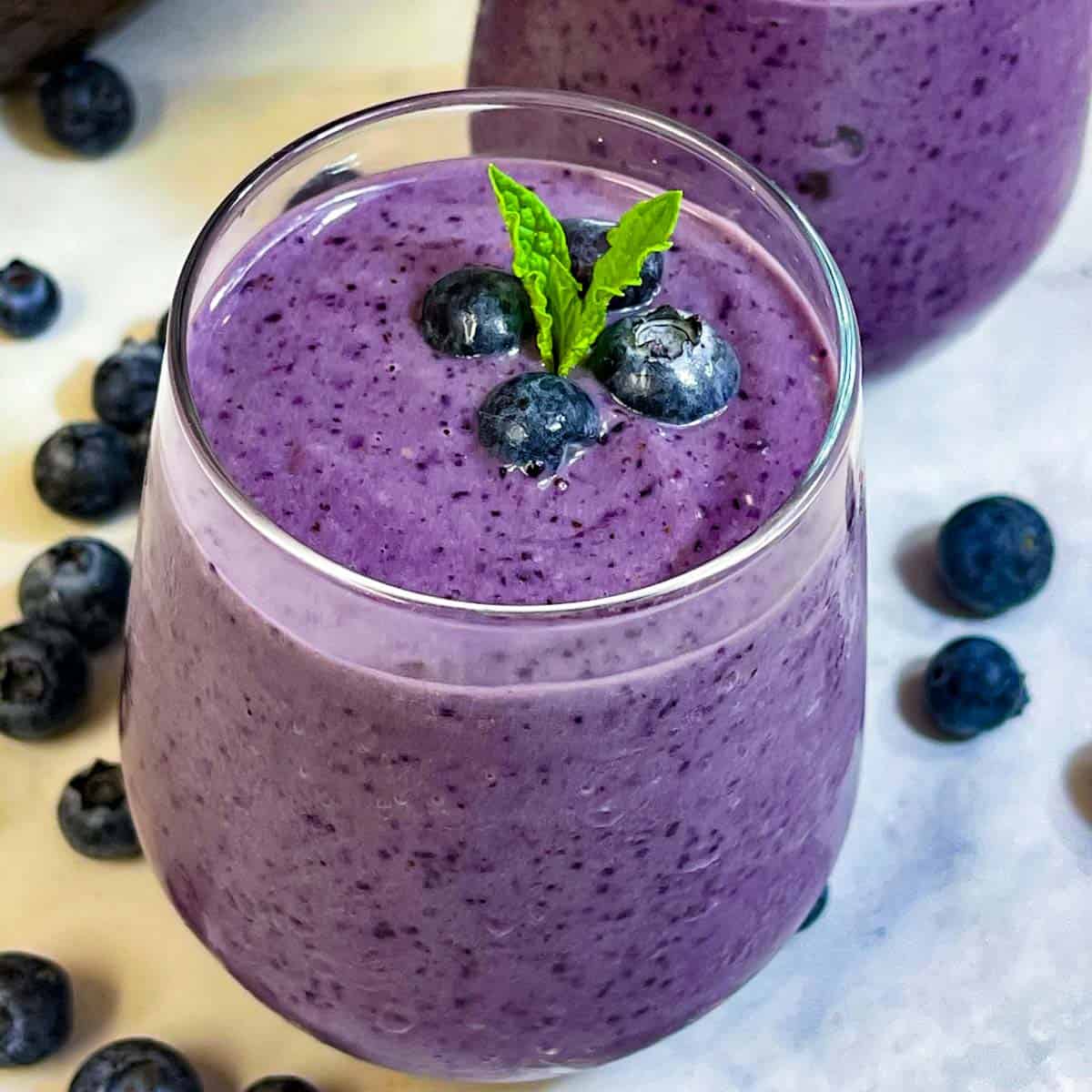blueberry avocado smoothie served in glasses topped with mint leaf and blueberries