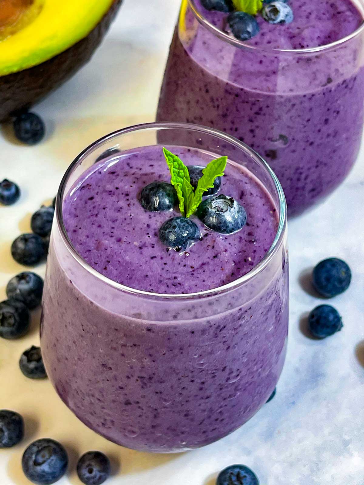 blueberry avocado smoothie served in glasses topped with mint leaf and blueberries