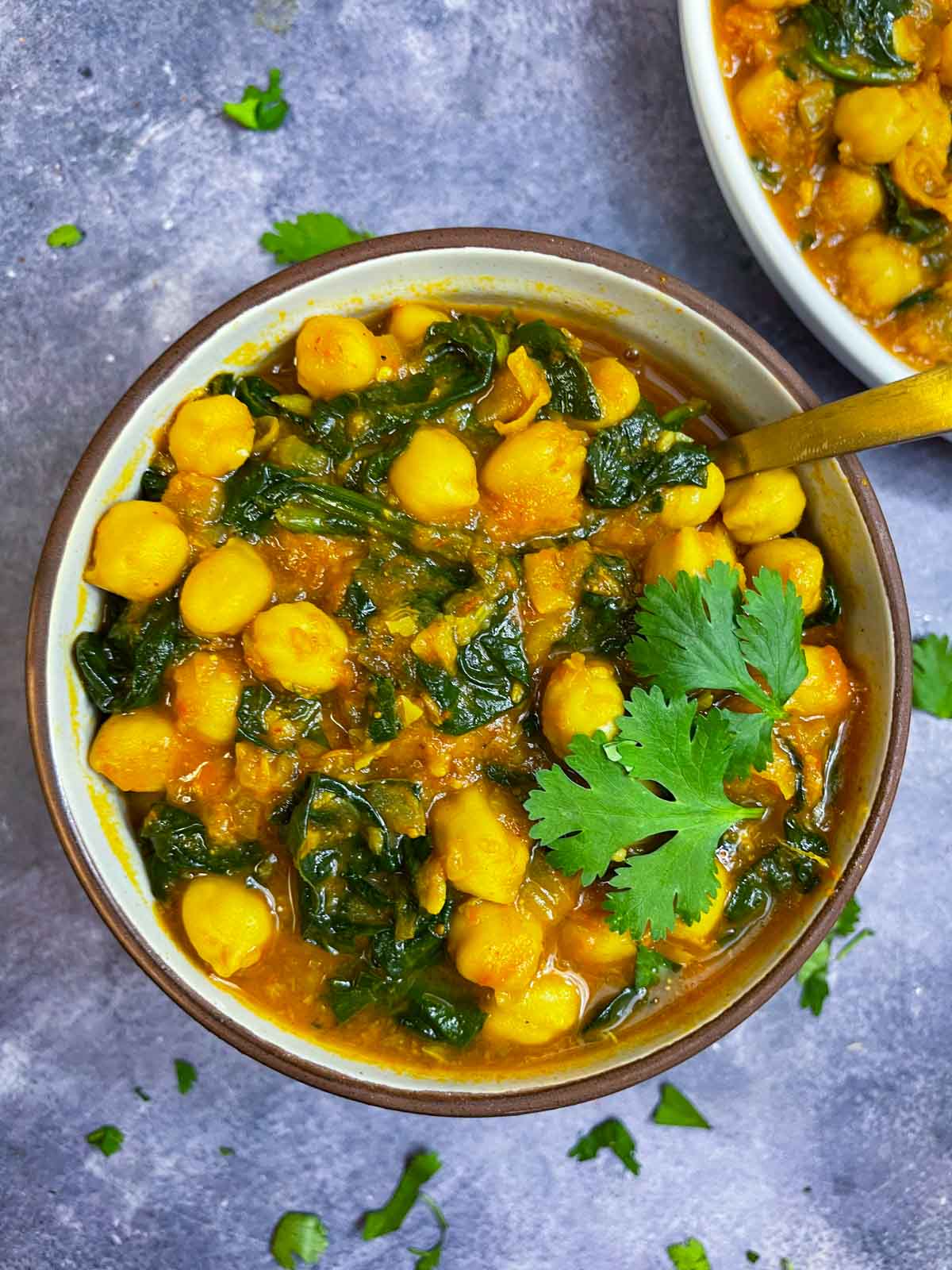 chickpea curry with spinach served in a bowl garnished with cilantro and has a spoon