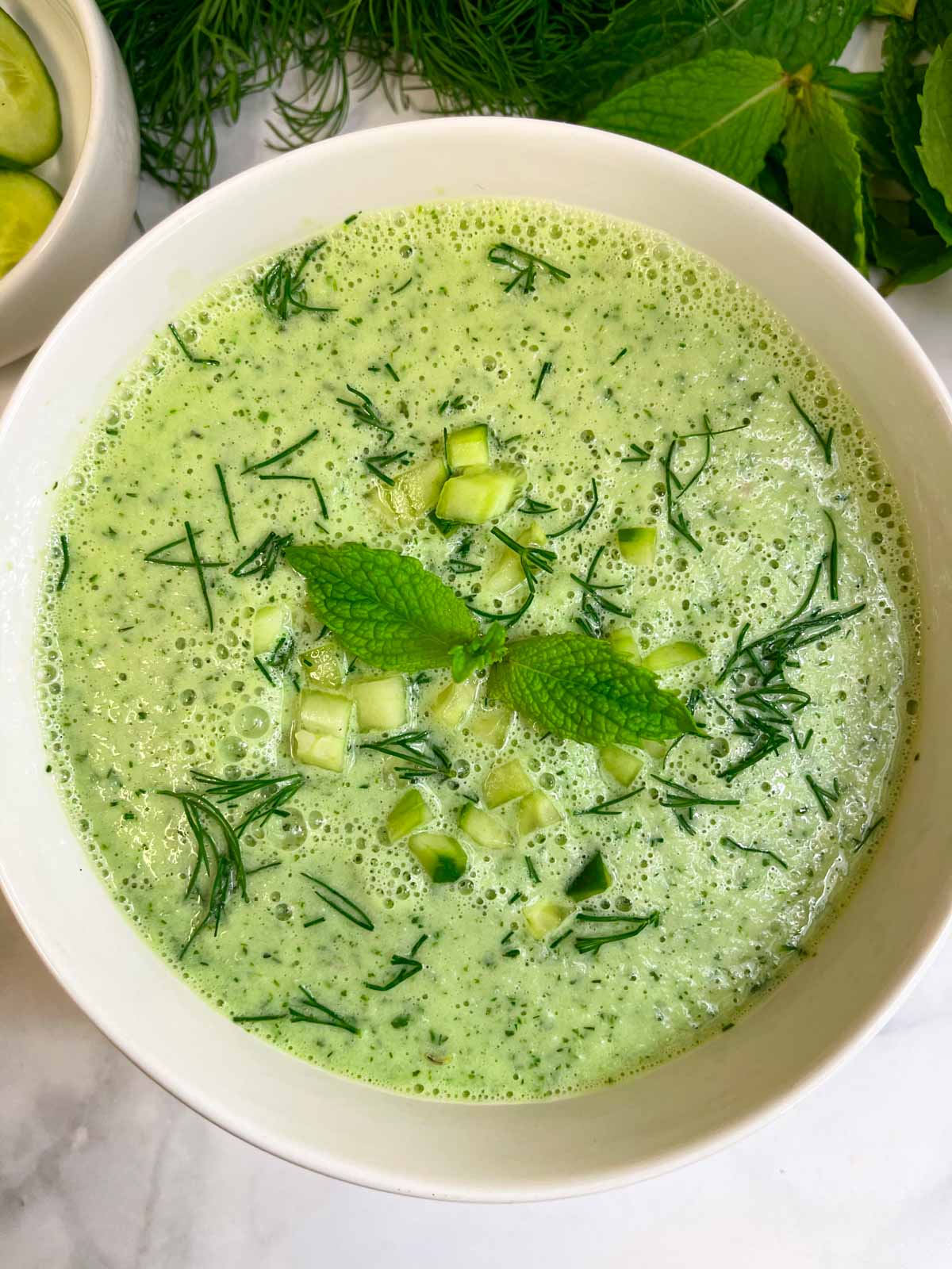 cold cucumber soup served in a bowl garnished with chopped cucumbers, dill leaves