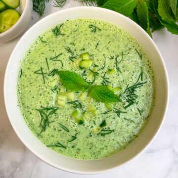 cold cucumber soup served in a bowl garnished with chopped cucumbers, dill leaves