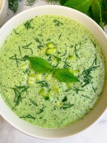 cold cucumber soup served in a bowl garnished with chopped cucumbers, dill leaves