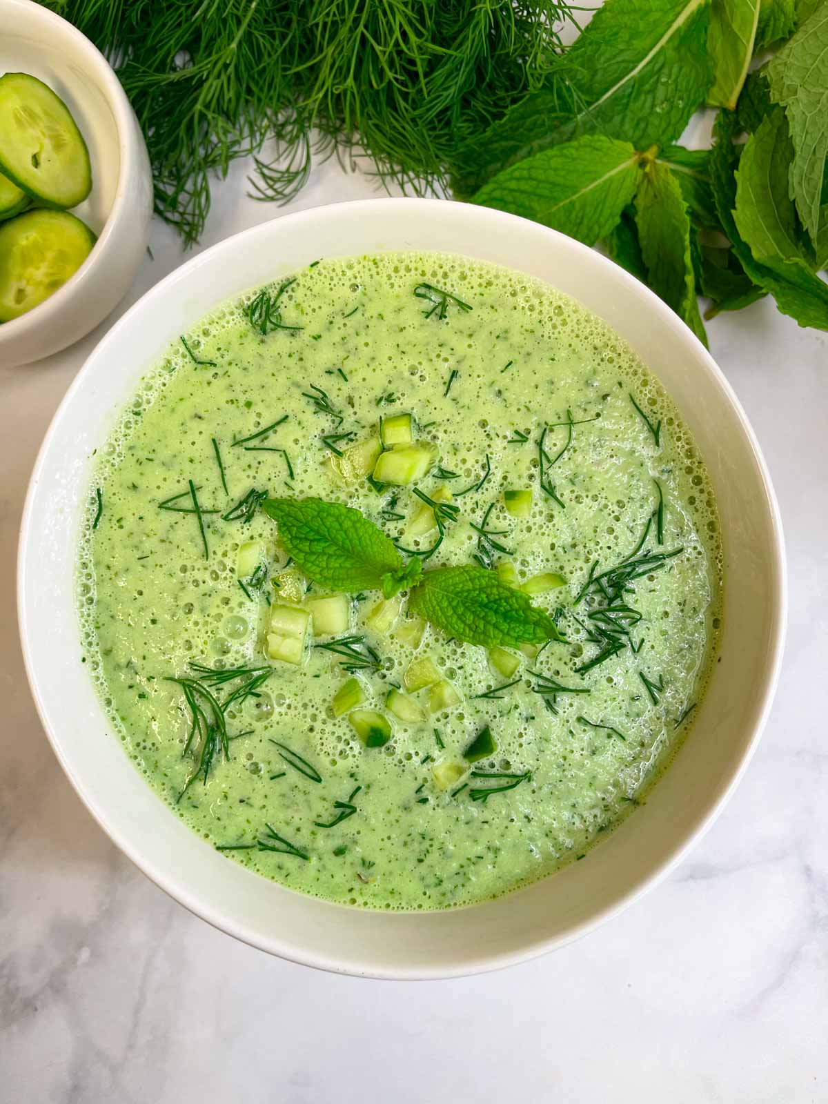 cold cucumber soup served in a bowl garnished with chopped cucumbers, dill leaves