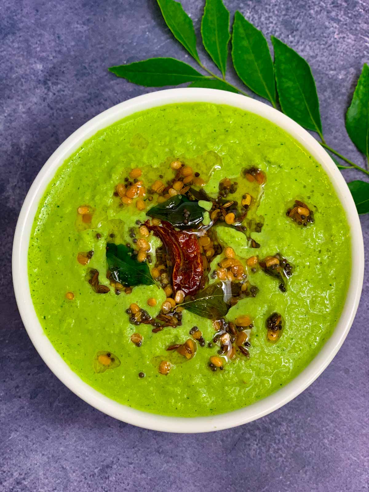 coriander coconut chutney served in a bowl with tempering on the top and curry leaves on the side