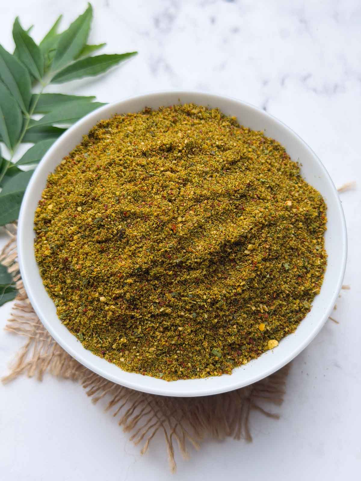 Curry leaves chutney powder in a white bowl with curry leaves stalks on the side for garnish.