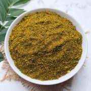Curry leaves chutney powder in a white bowl with curry leaves stalks on the side for garnish.