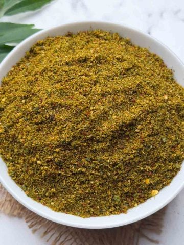 Curry leaves chutney powder in a white bowl with curry leaves stalks on the side for garnish.