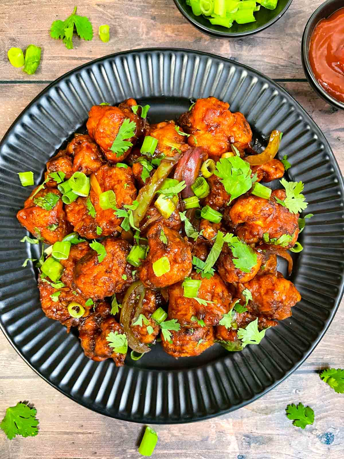 gobi manchurian served on a plate garnished with green onions and cilantro with side of tomato ketchup